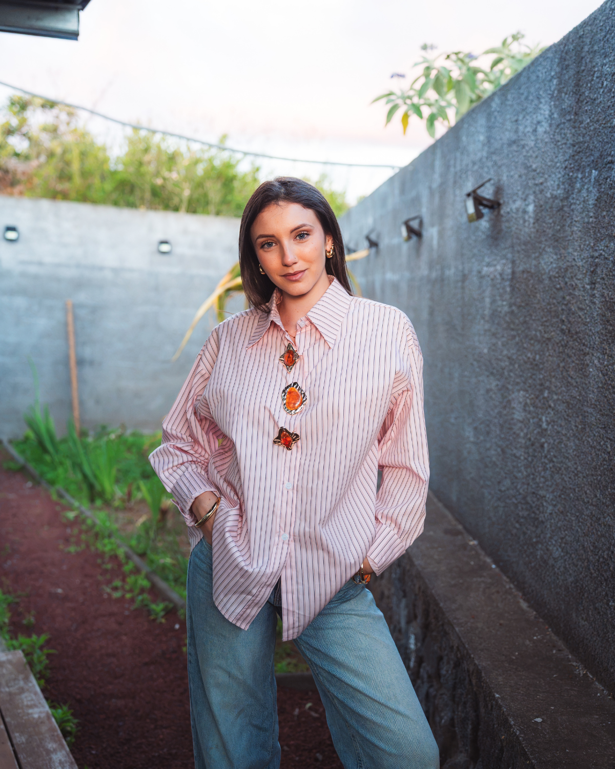 Femme portant un chemisier oversize rayé rose à boutons bijoux orange avec un jean large